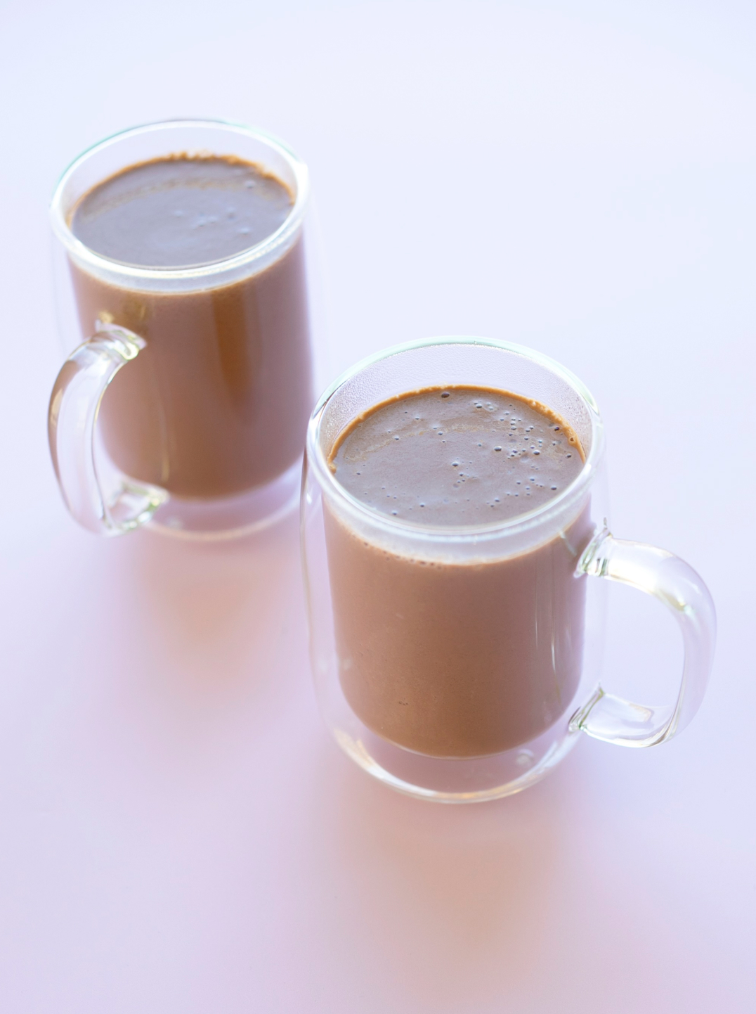 two glass mugs filled with tahini spiced hot chocolate on pale purple background