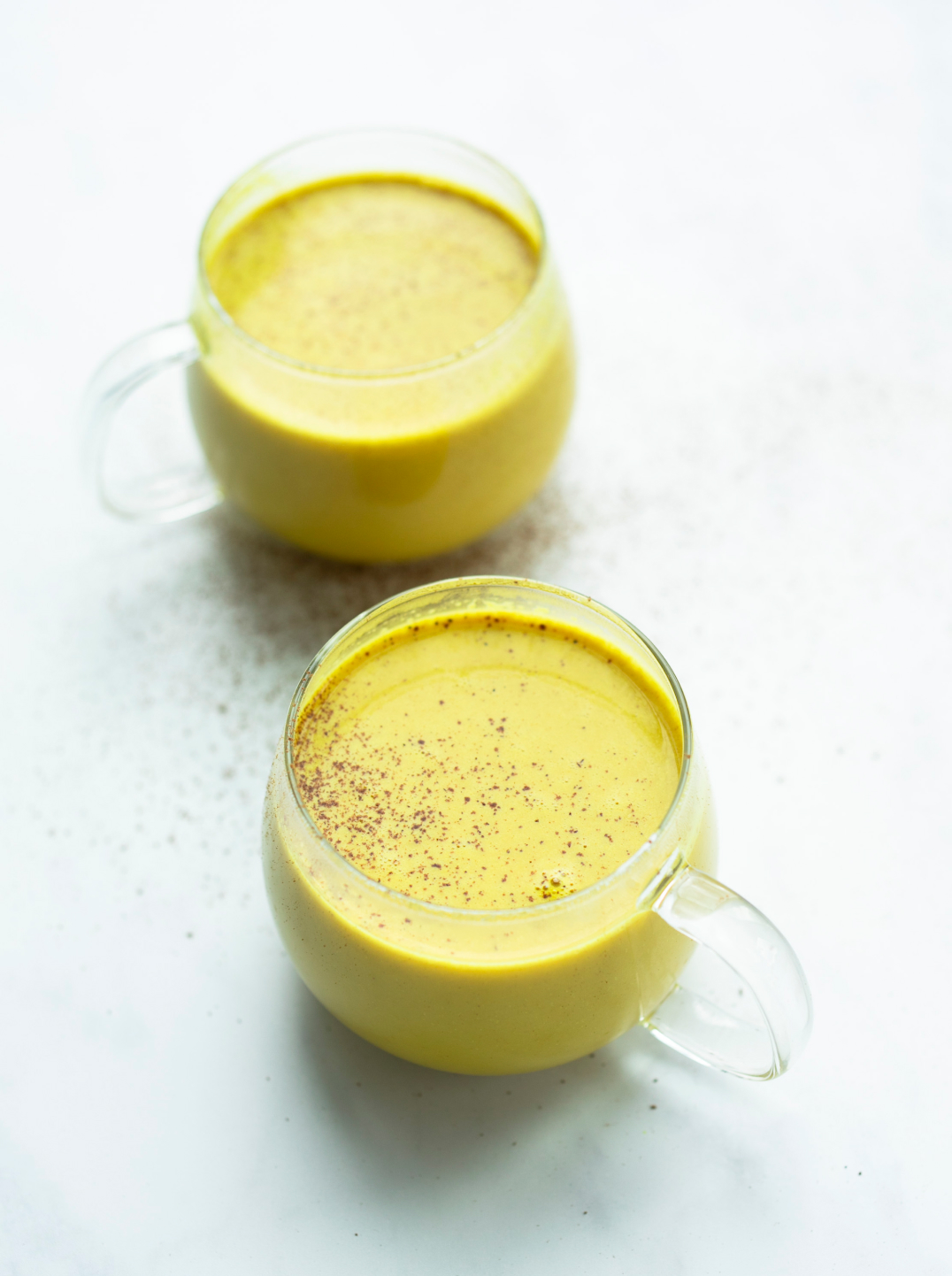 two glass mugs filled with rich golden yellow moon milk on a marble surface