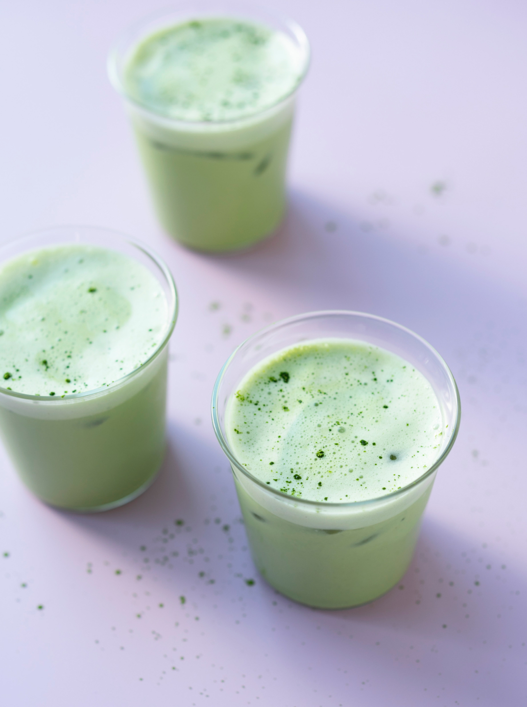 3 glasses of frothy green matcha morning milk on a pale purple background
