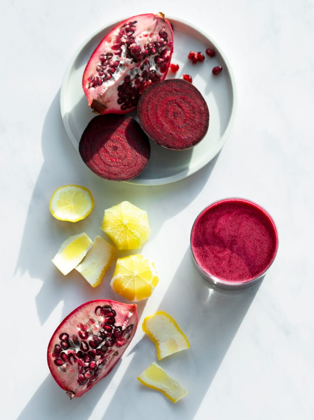 Sliced fresh beets and pomegranate  with fresh lemon and a glass filled with beet red beet blitz juice