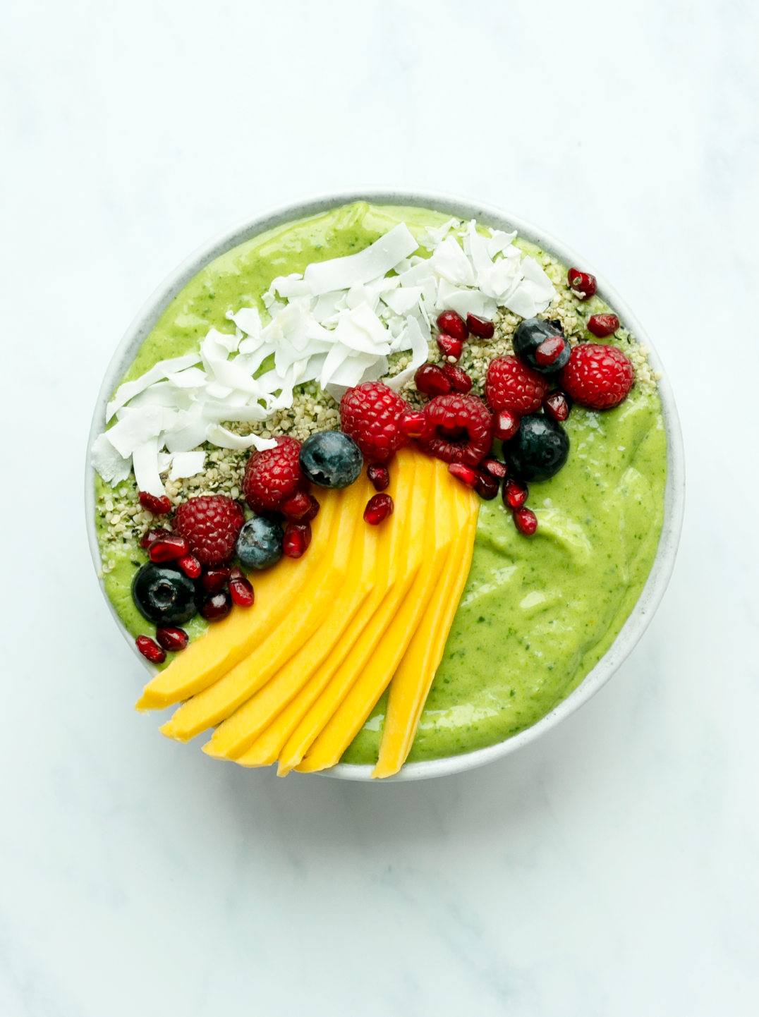 A beautiful green smoothie bowl topped with nmango slices fresh berries and coconut
