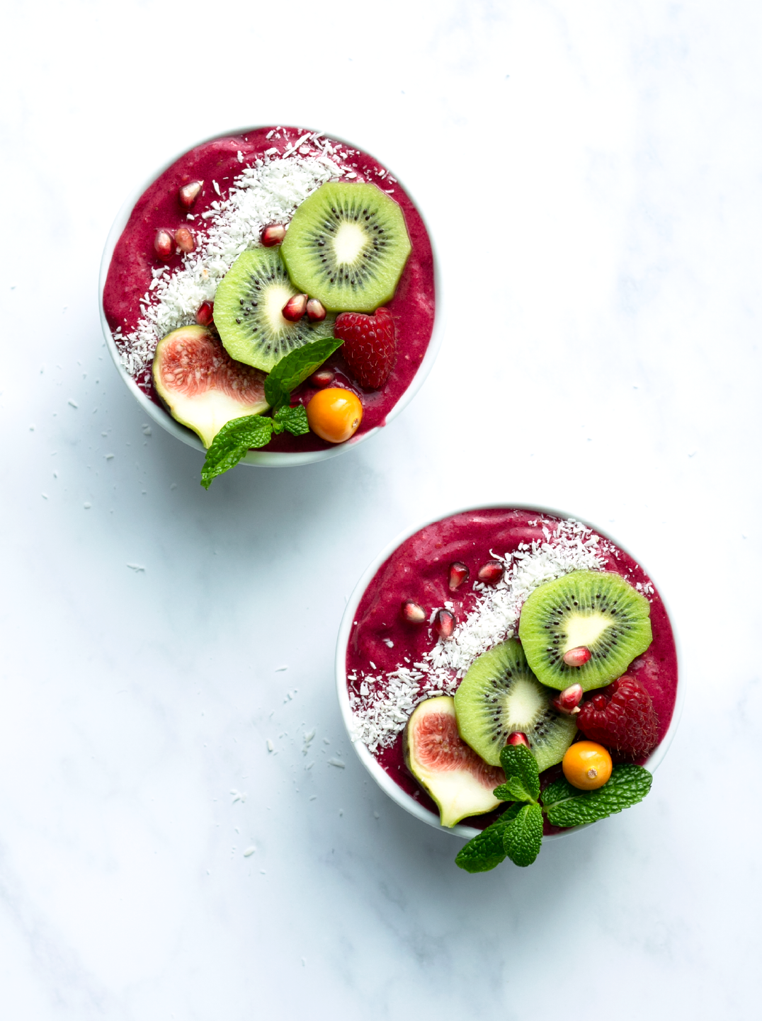 Two bowls filled with deep red smoothie and topped with sliced kiwi fig and shredded coconut