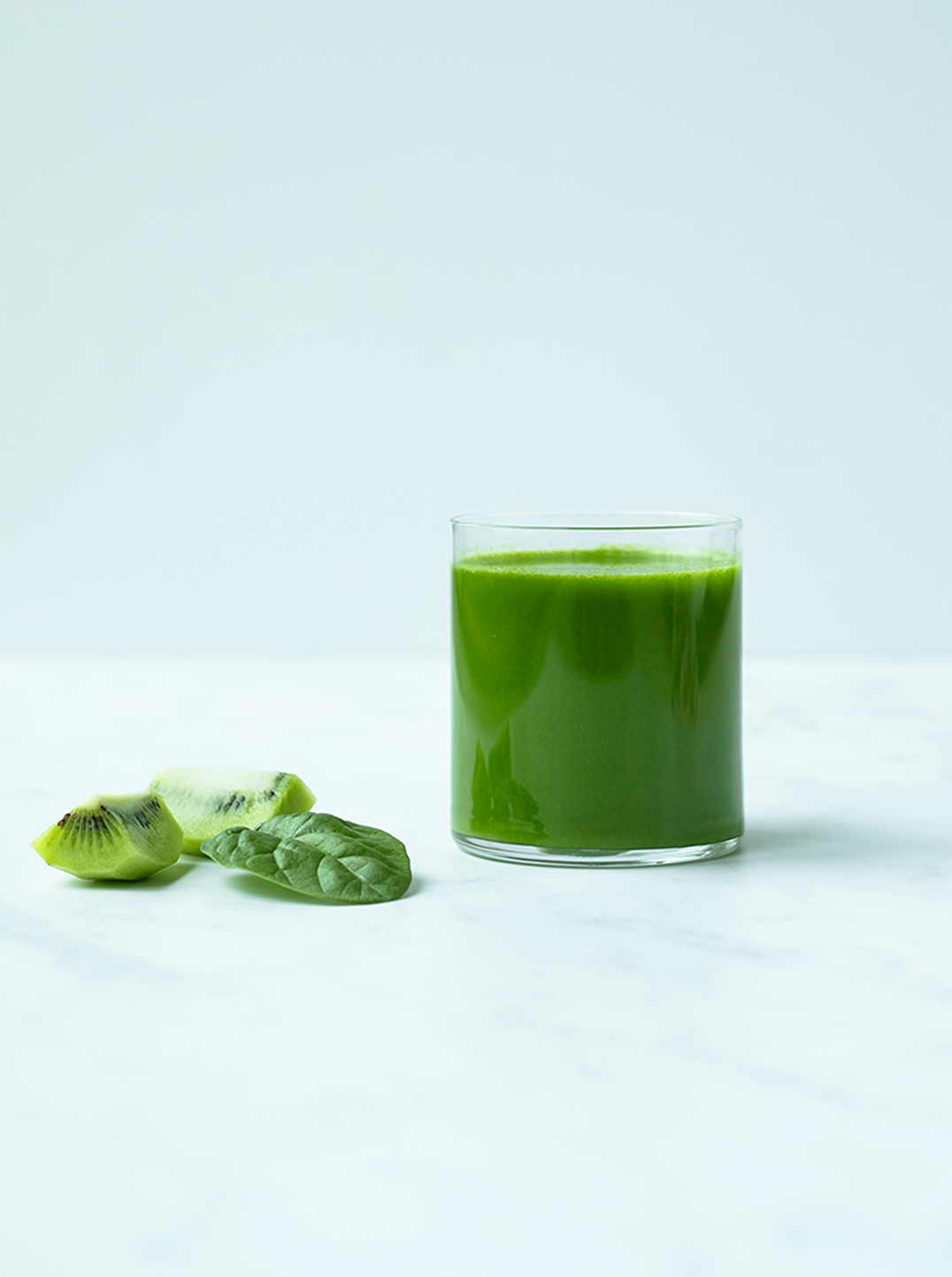 a glass of kiwi green juice with a few spinach leaves
