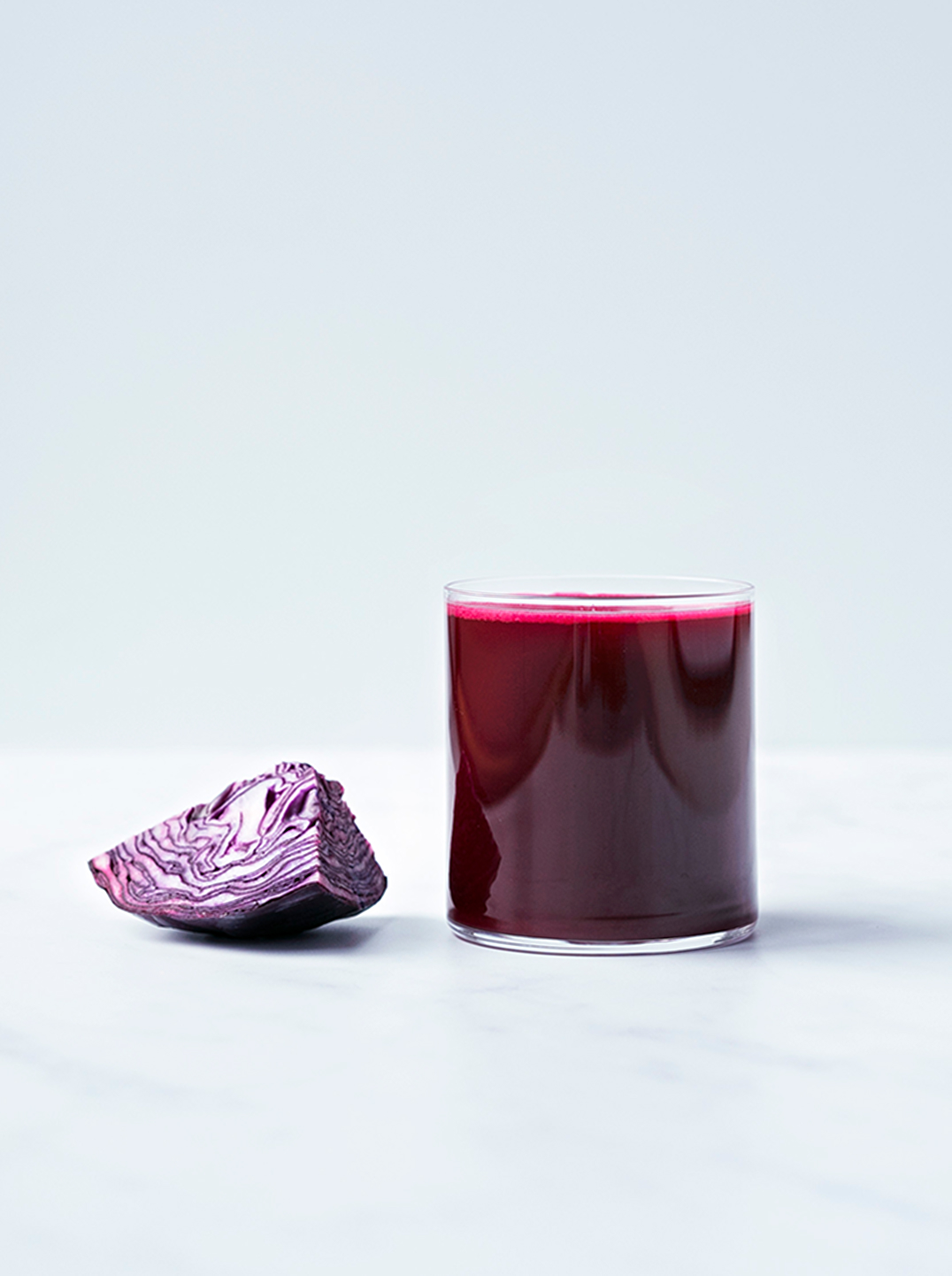 a glass of cabbage crush juice with a piece of red cabbage