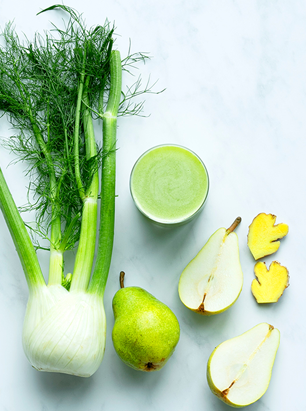 a glass of spicy pear juice with a fennel bulb green pears and a slice of ginger
