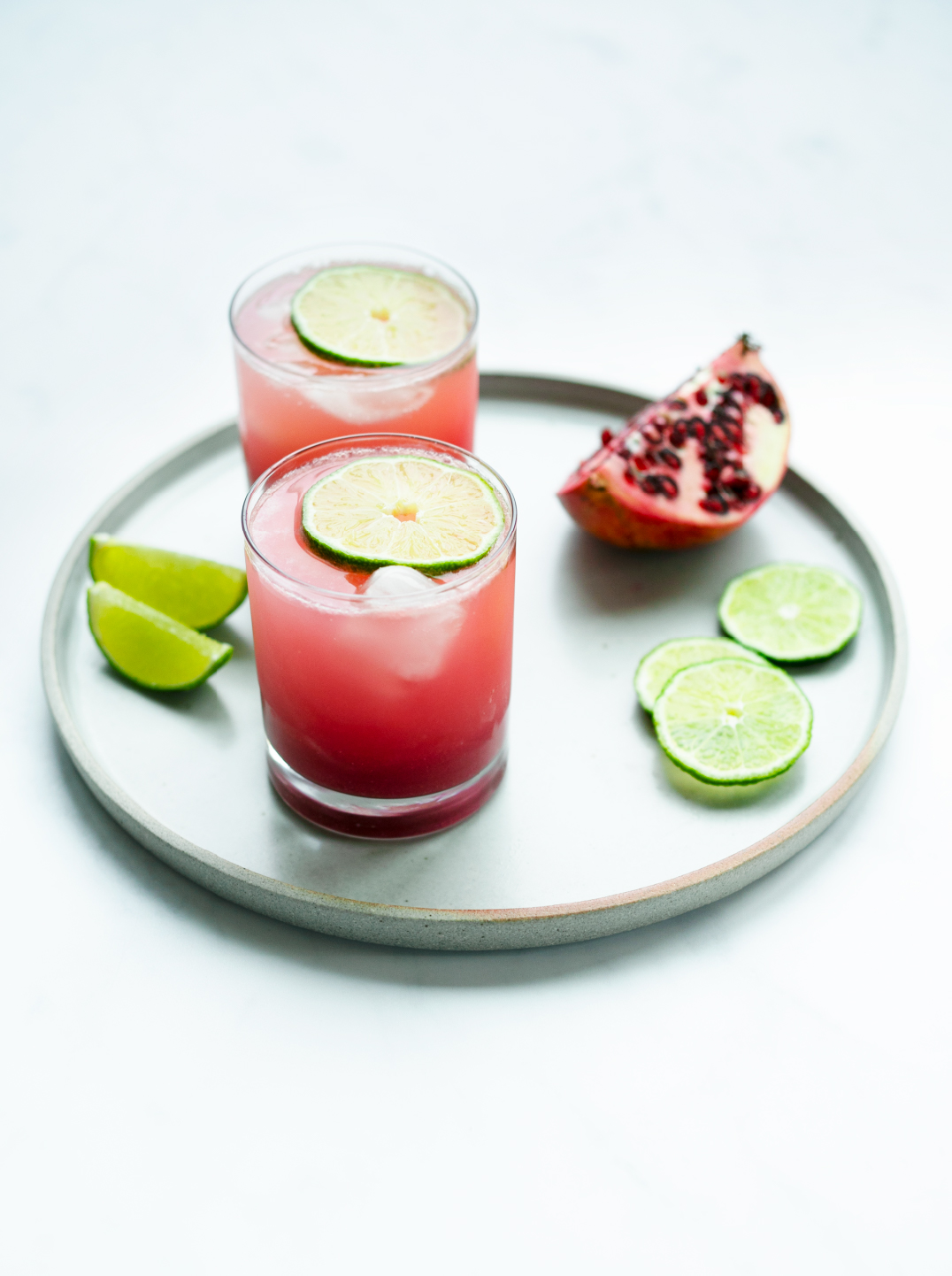 2 glasses of pomegranate glow juice on a plate with lime and pomegranate wedges.