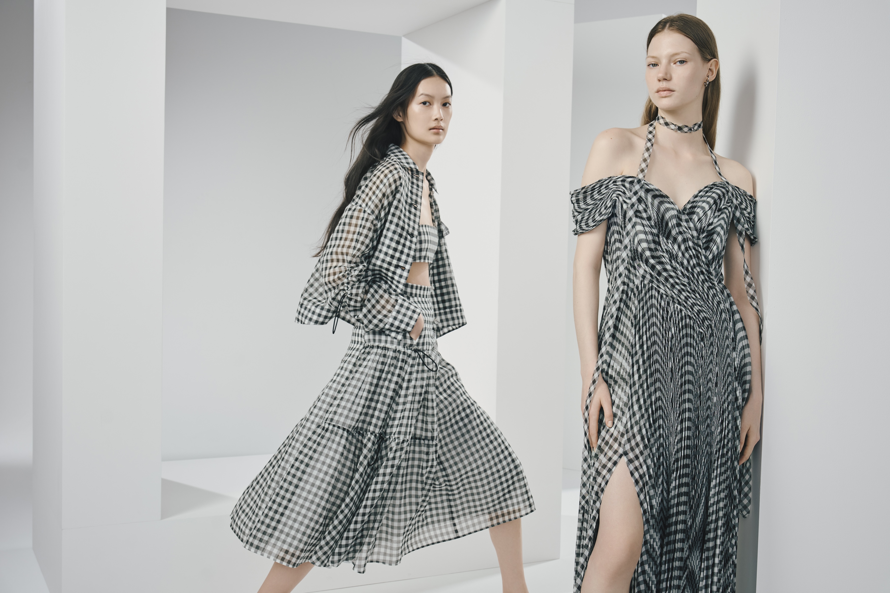 Two women wearing black and white checkered outfits, one in a matching skirt and jacket set, the other in an off-shoulder dress with a slit.