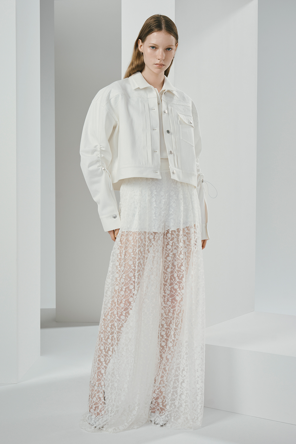 Model is wearing a white lace skirt paired with a matching white jacket.