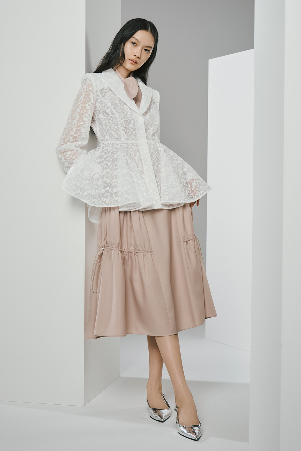 Model is wearing a white jacket and a pink skirt.