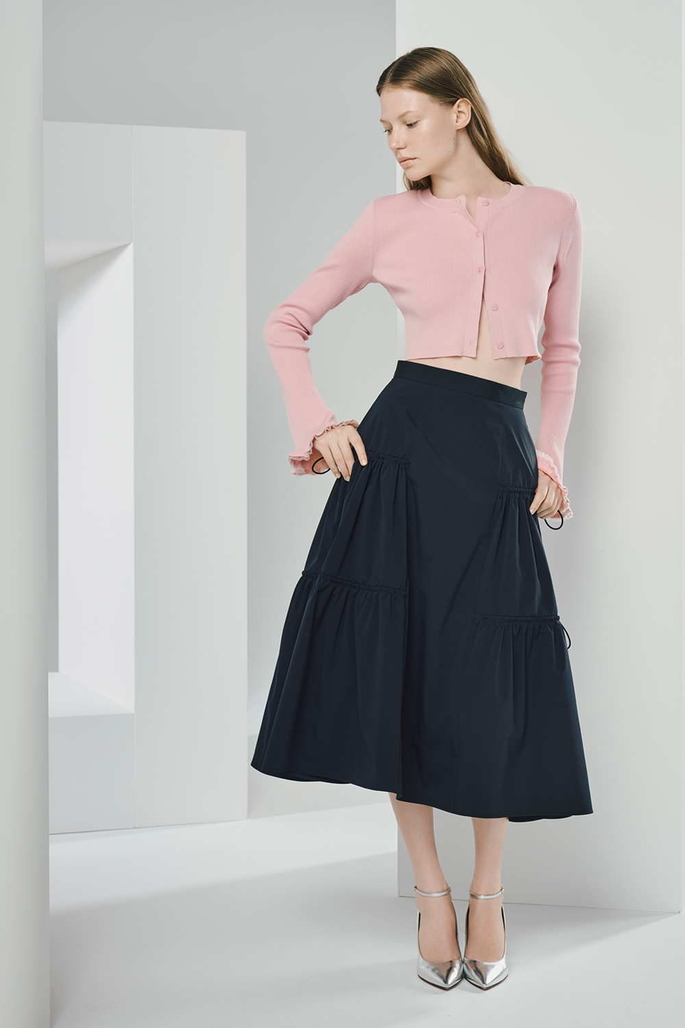 Model is wearing a pink cardigan and a black skirt.