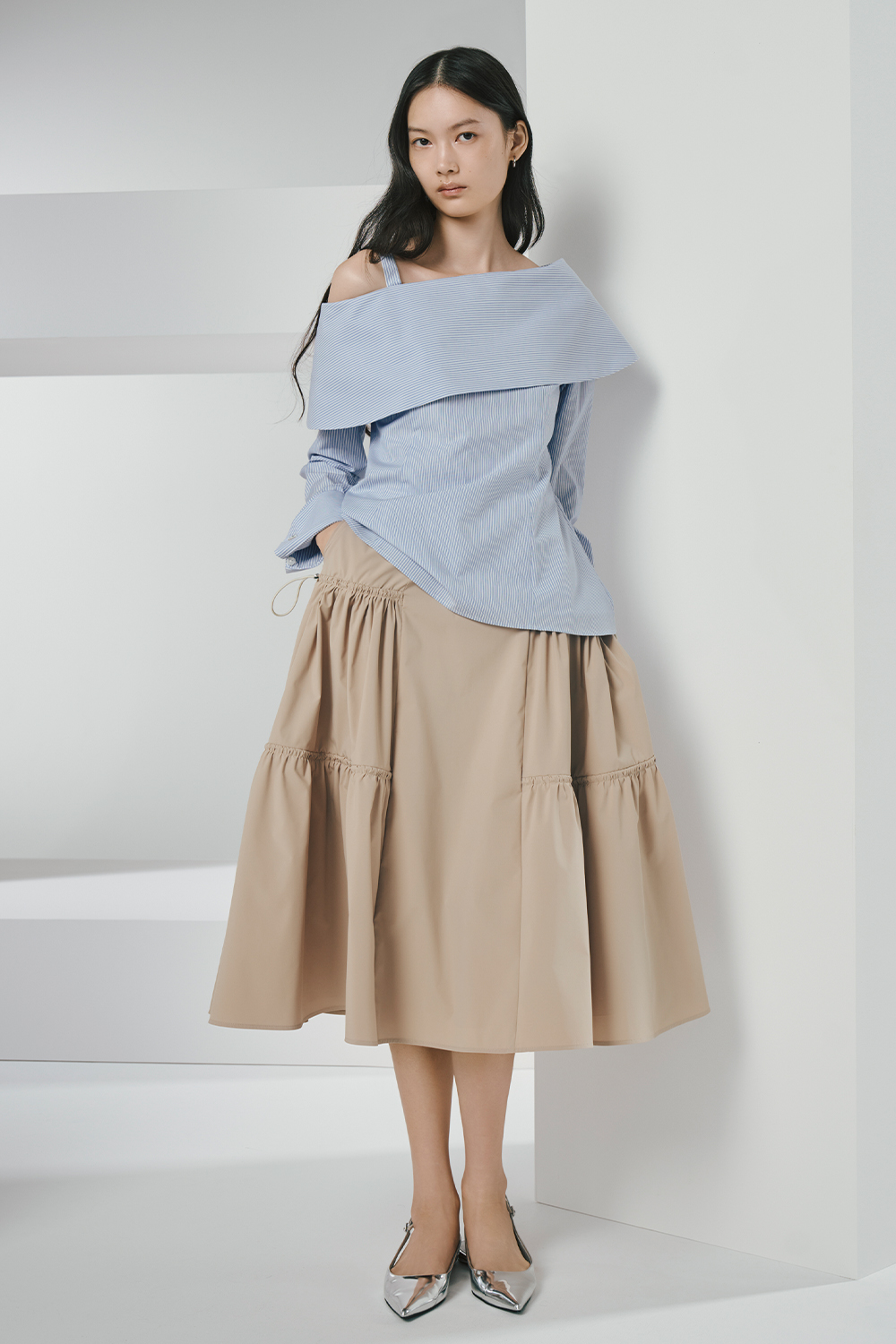Model is wearing a blue top and a beige skirt.