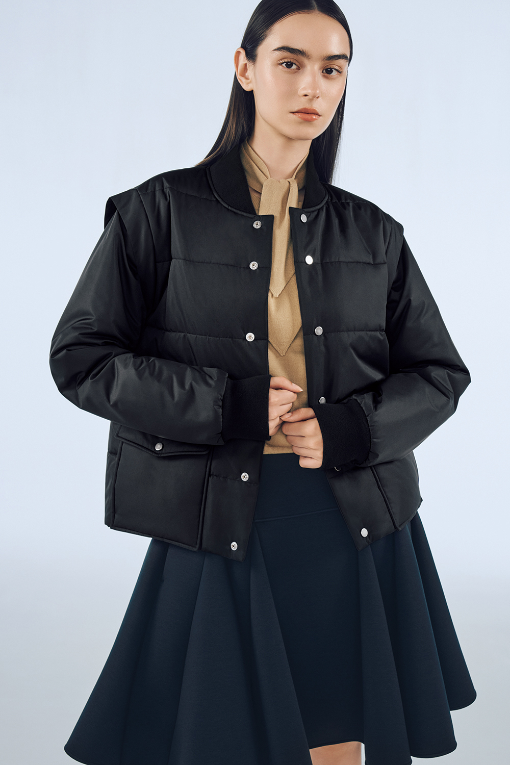 Model is wearing a black skirt and a black jacket over a beige top.