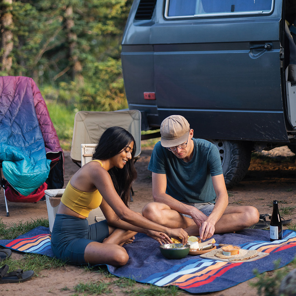 Two people enjoying a picnic using the Rumpl Everywhere Mat outside their camper van.