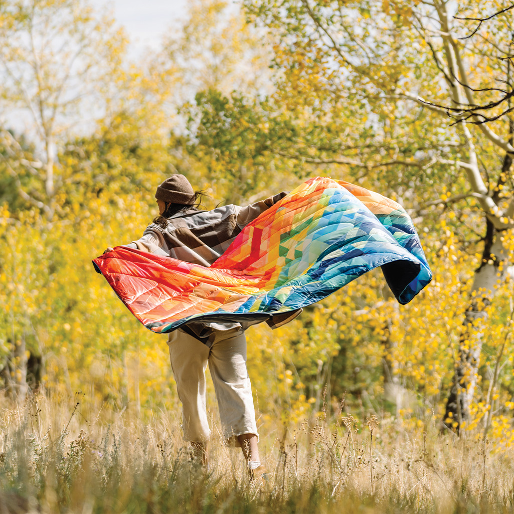 A person in the great outdoors, holding up a Geo print Rumpl Original Puffy Blanket.