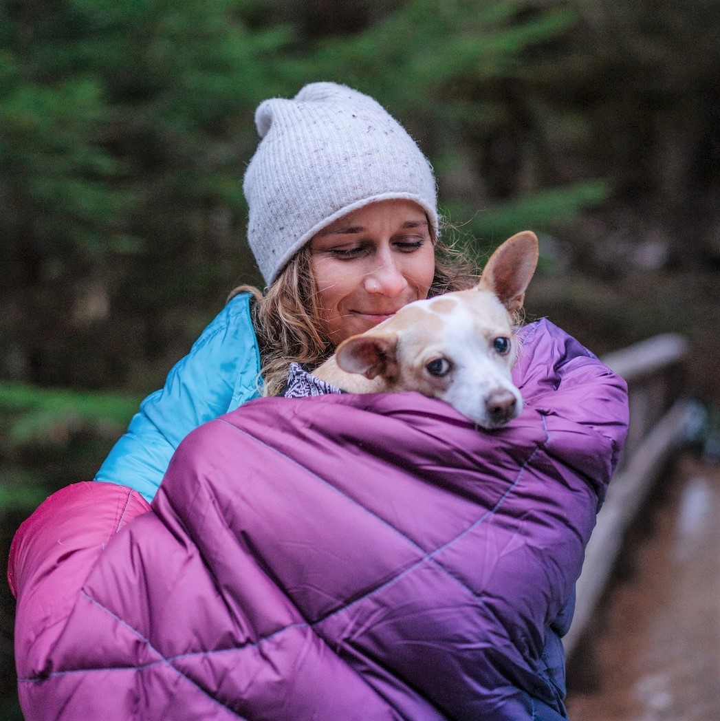A girl and her dog bundled up in a Rumpl Nanoloft Puffy Blanket