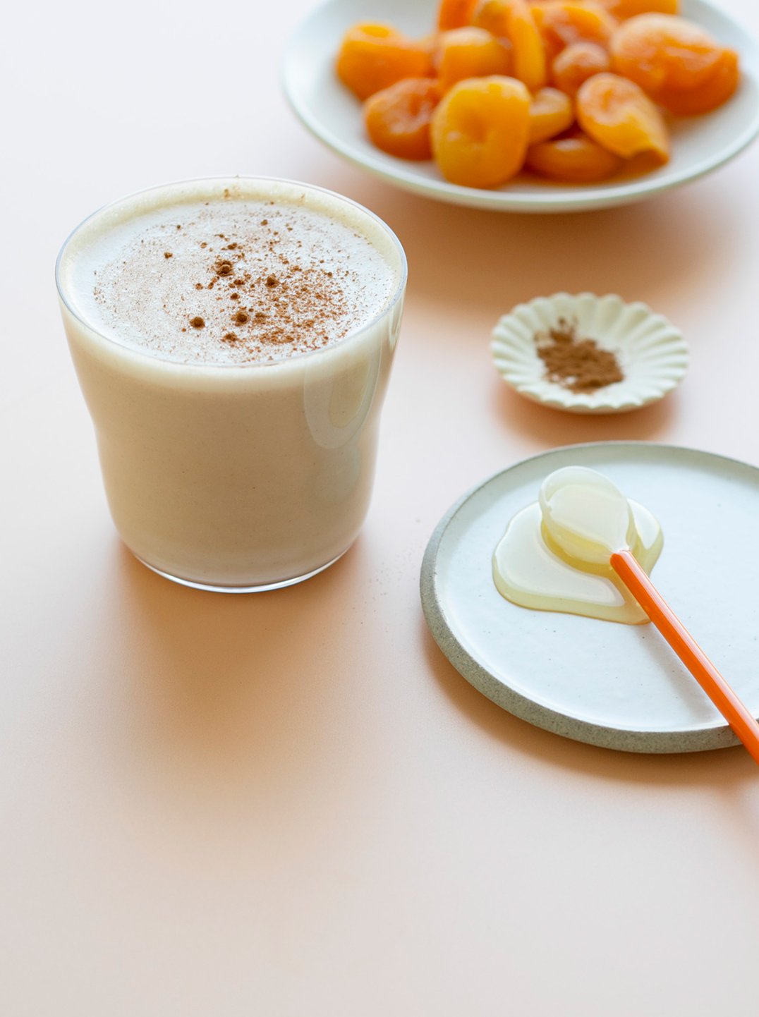 a glass of apricot almond milk with a bowl of dried apricots and a green plate with spoon