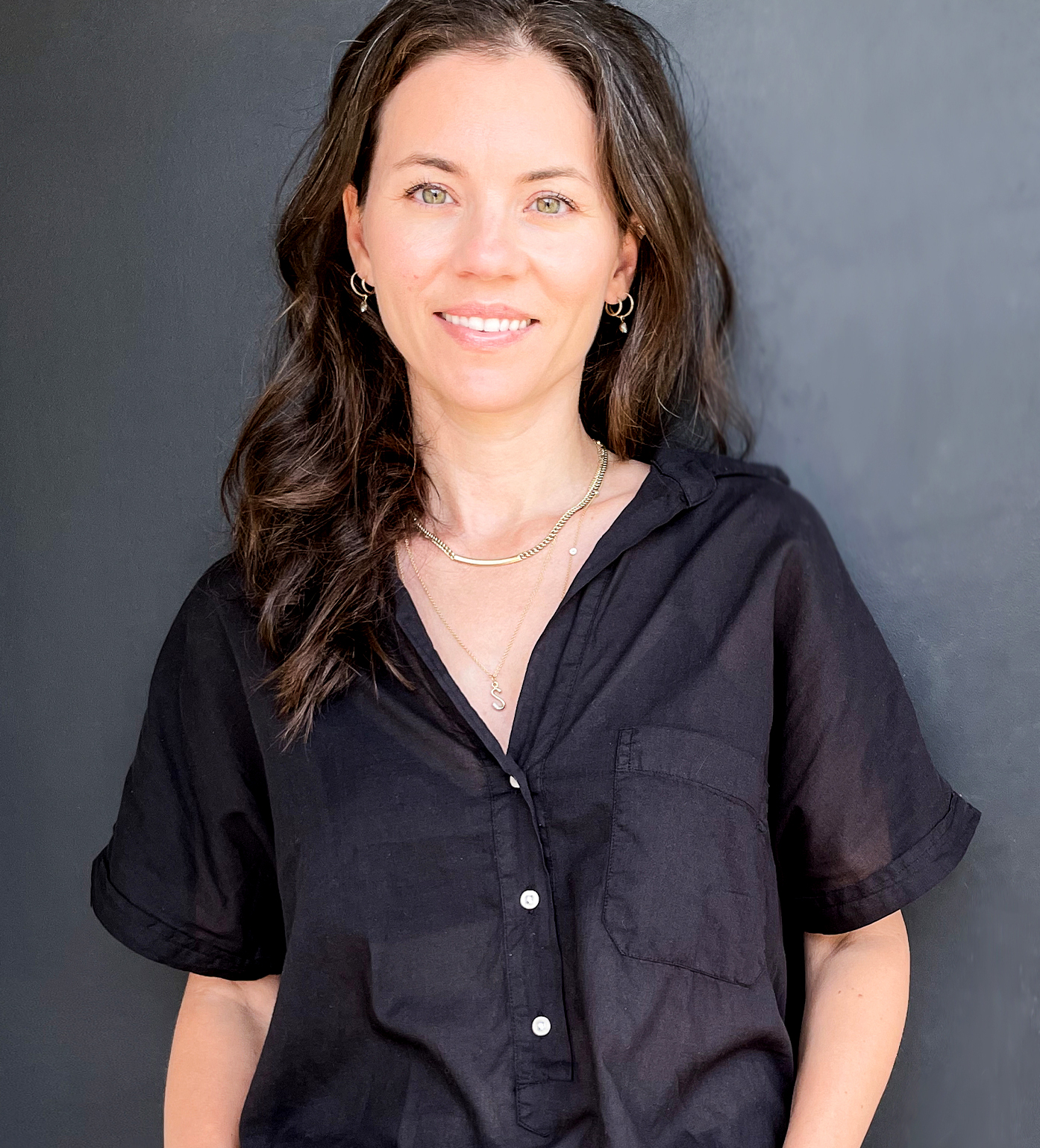 Portrait of Stacy Nolan. She has fair skin, light eyes, and nearly black hair. She is wearing a delicate chain necklace over a collared shirt with a deep neckline.