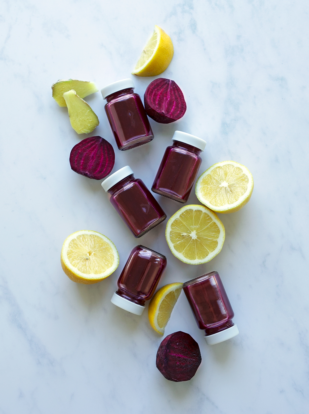 5 small bottles of beet power shot with lemon pieces and a slice of ginger
