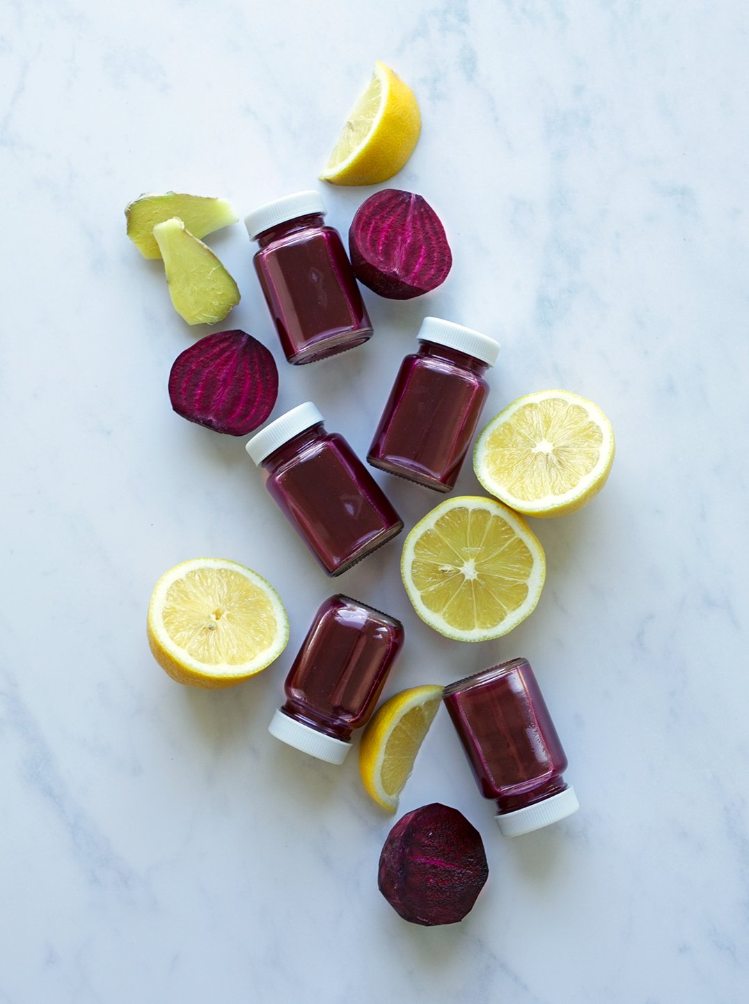 5 small bottles of beet power shot with lemon pieces and a slice of ginger