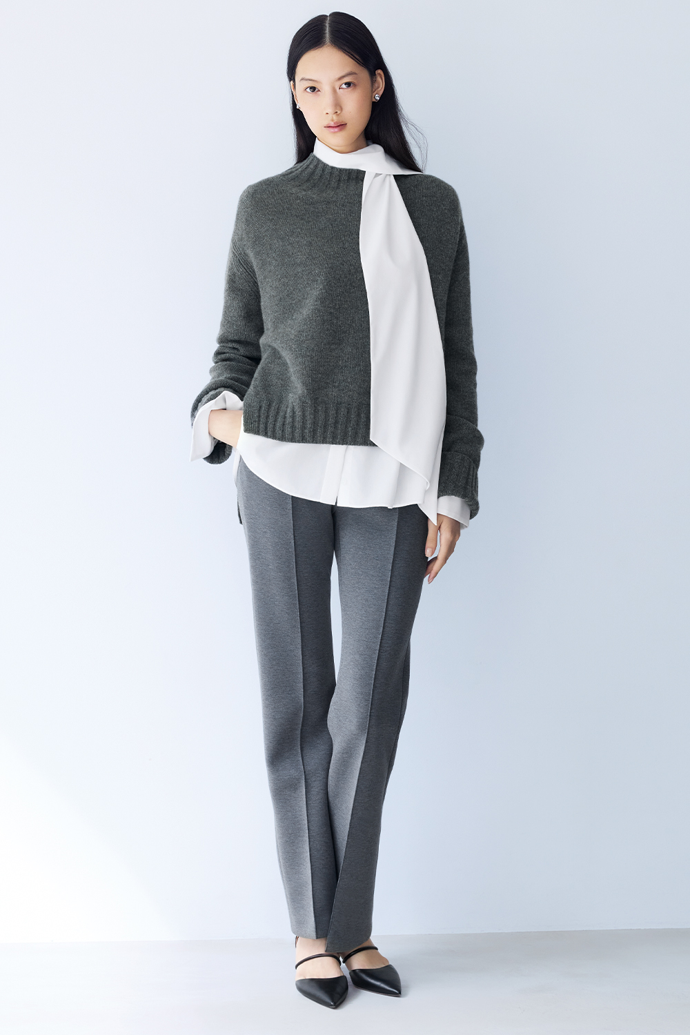 Model is wearing grey pants and a grey sweater over a white shirt.