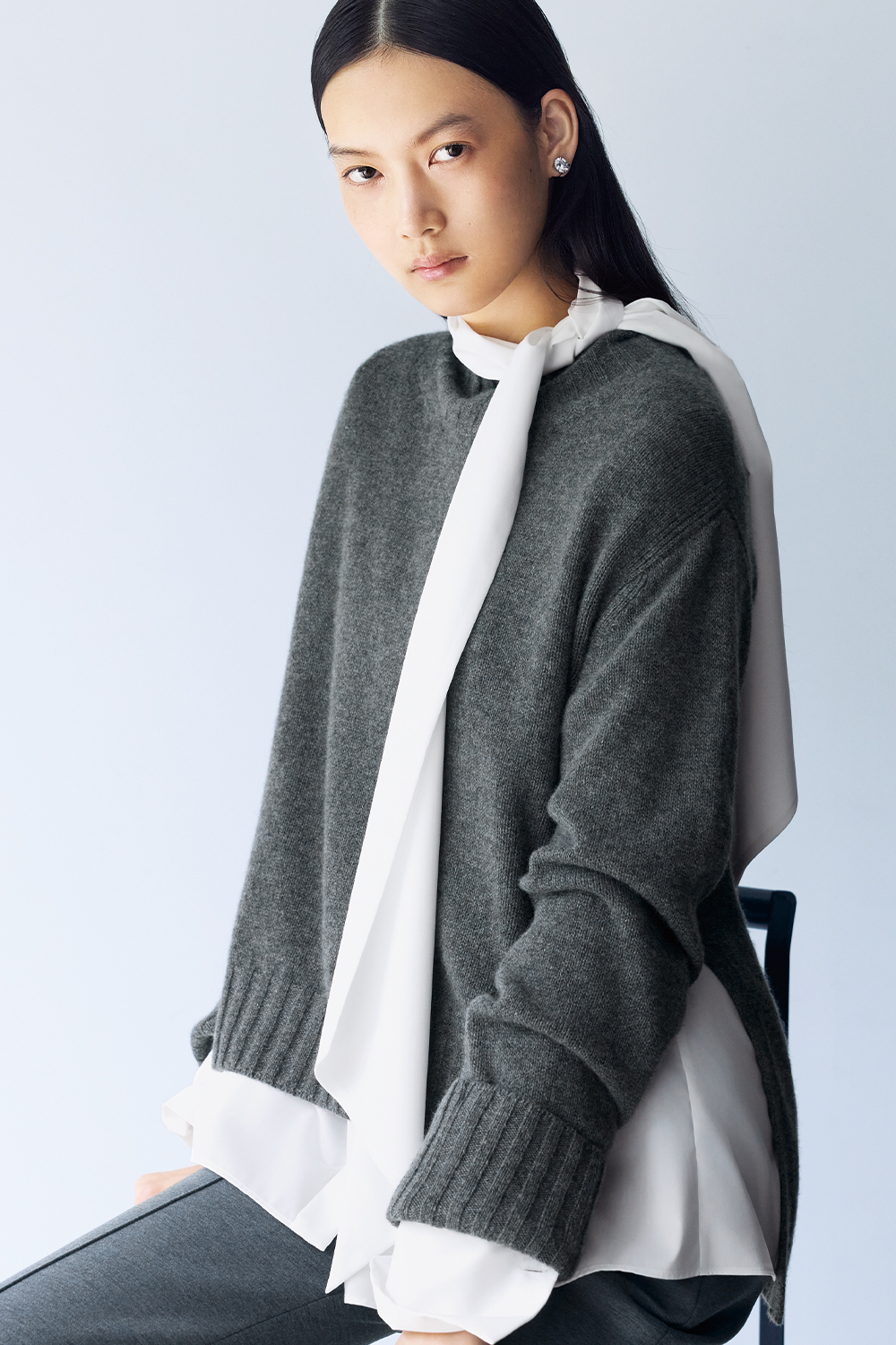 Model is wearing grey pants and a grey sweater over a white shirt.
