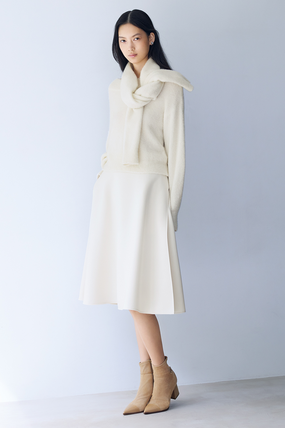 Model is wearing a white sweater, skirt and beige boots.