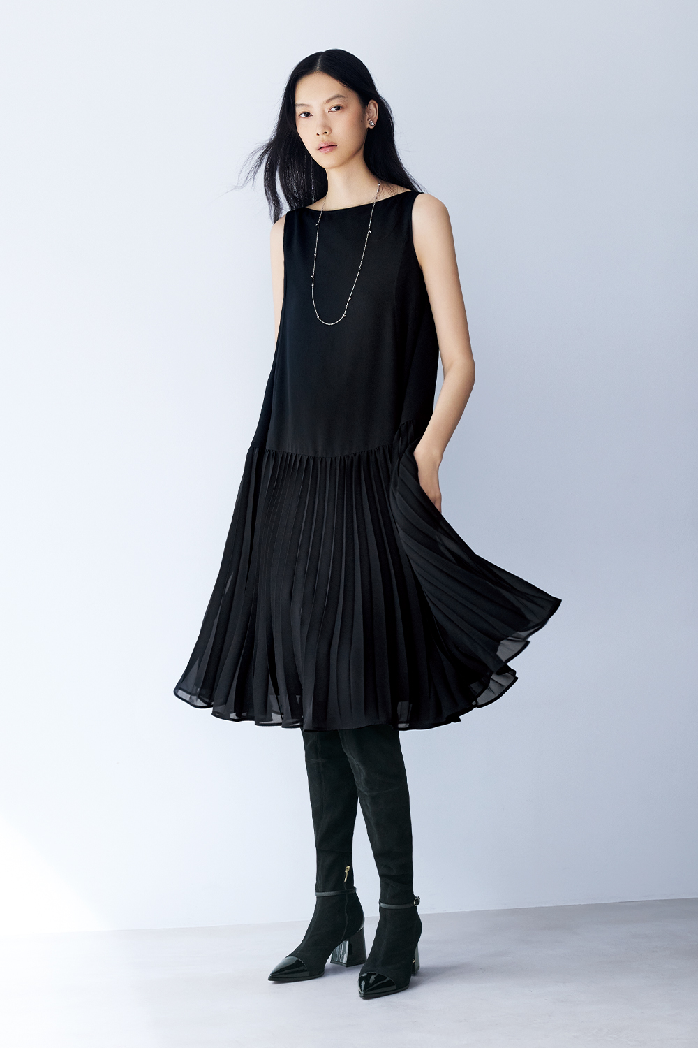 Model is wearing black boots and a dress with a silver necklace.