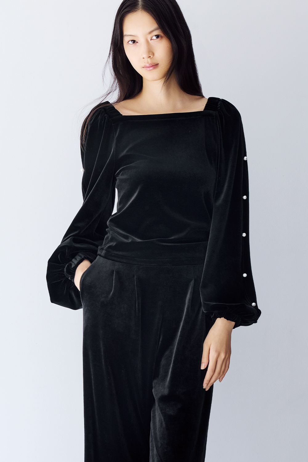 Model is wearing a black velvet top with long sleeves and black pants.