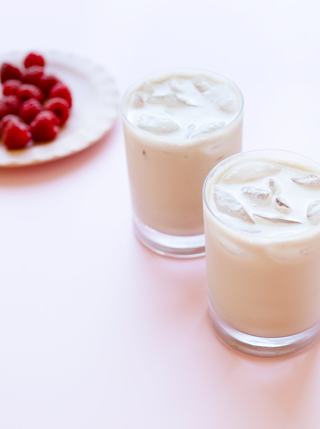 2 glasses of Pistachio & Almond Berry Boost over ice with a plate of raspberries in the background
