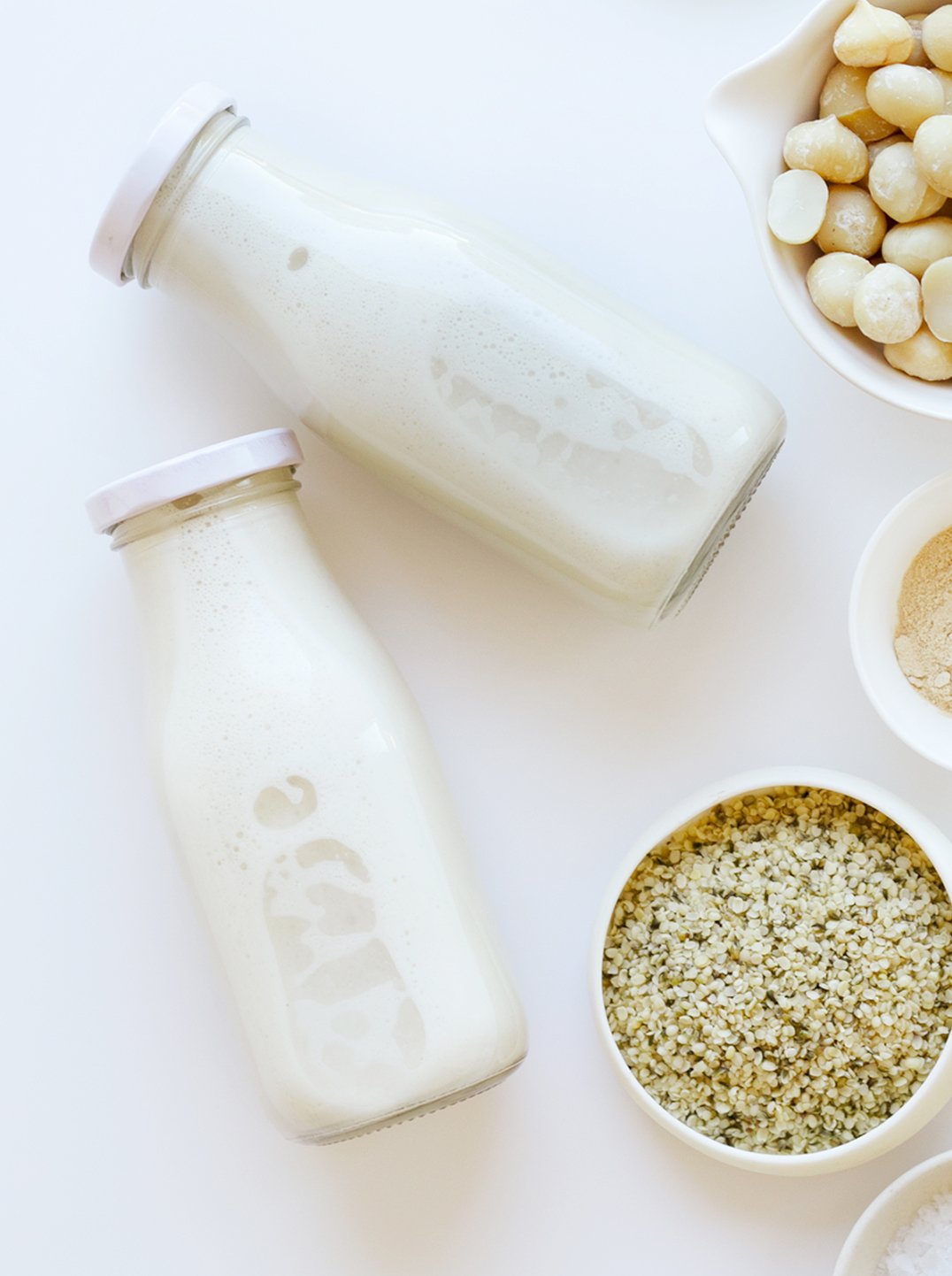 two bottles of maca energy milk with 3 small bowls of ingredients.
