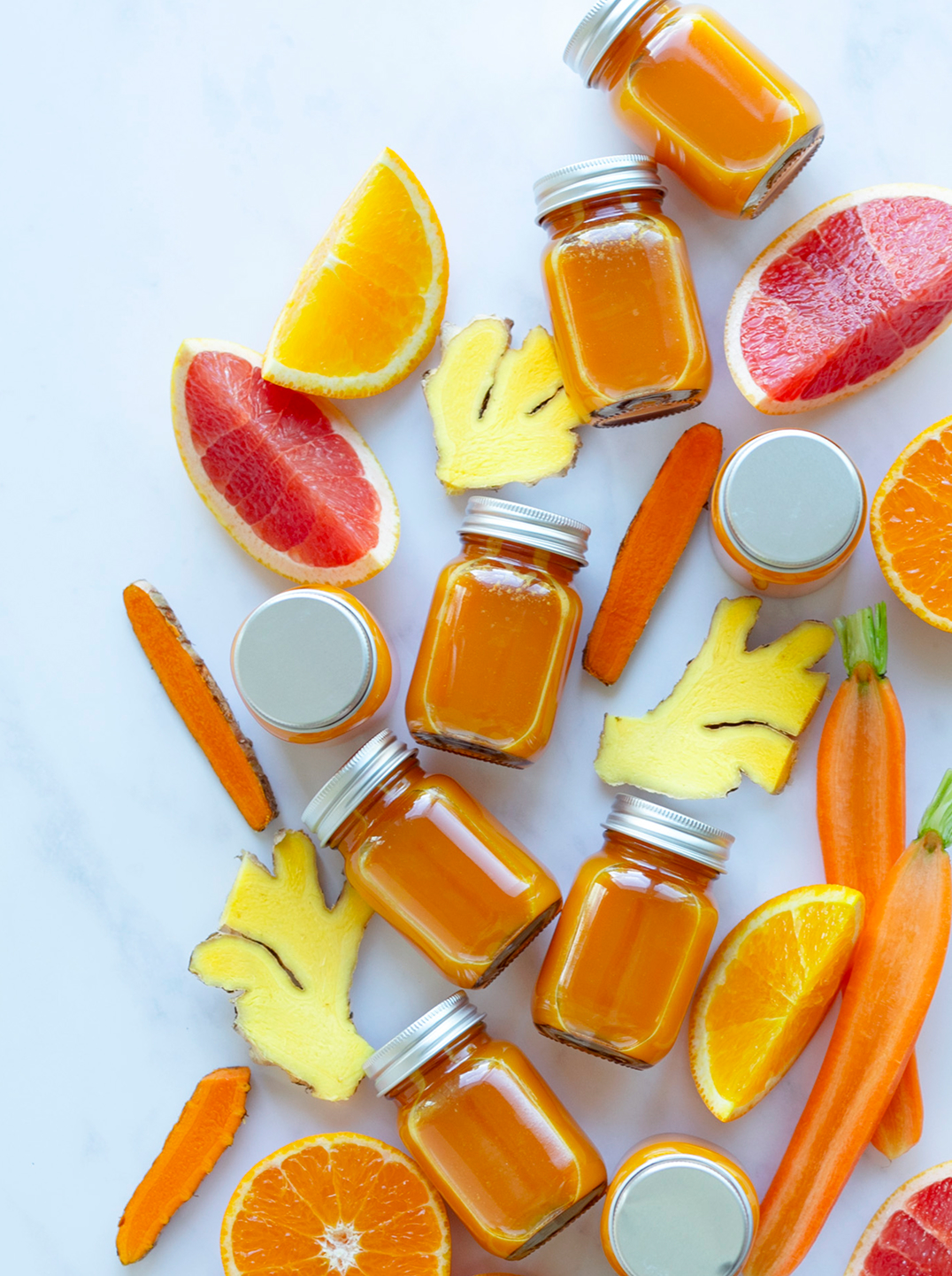 An array of small of bright orange recovery shot bottles with carrots and ginger
