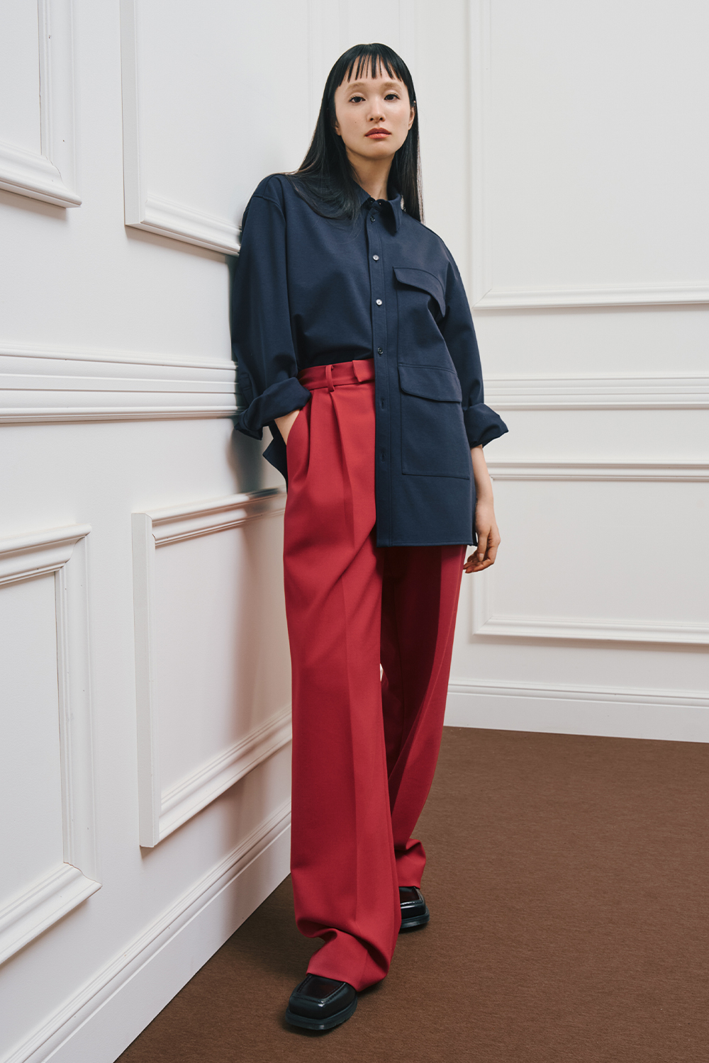 A model is wearing a navy button-up shirt with oversized pockets, paired with high-waisted red wide-leg pants and black shoes.