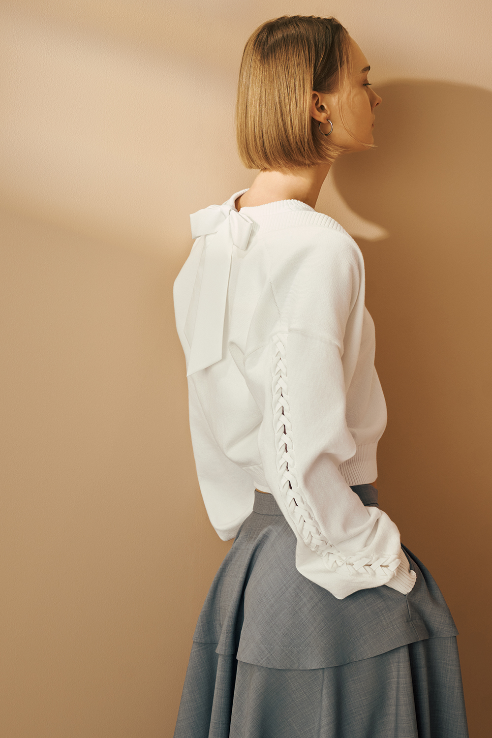 Model is wearing a white long-sleeve top with a layered detail and a gray midi flared skirt.