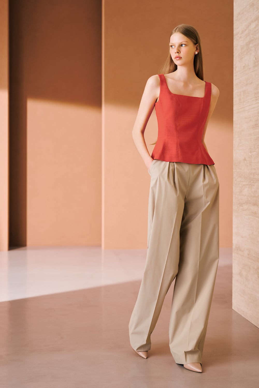 A model is wearing a coral sleeveless top with a square neckline, paired with beige wide-leg trousers.