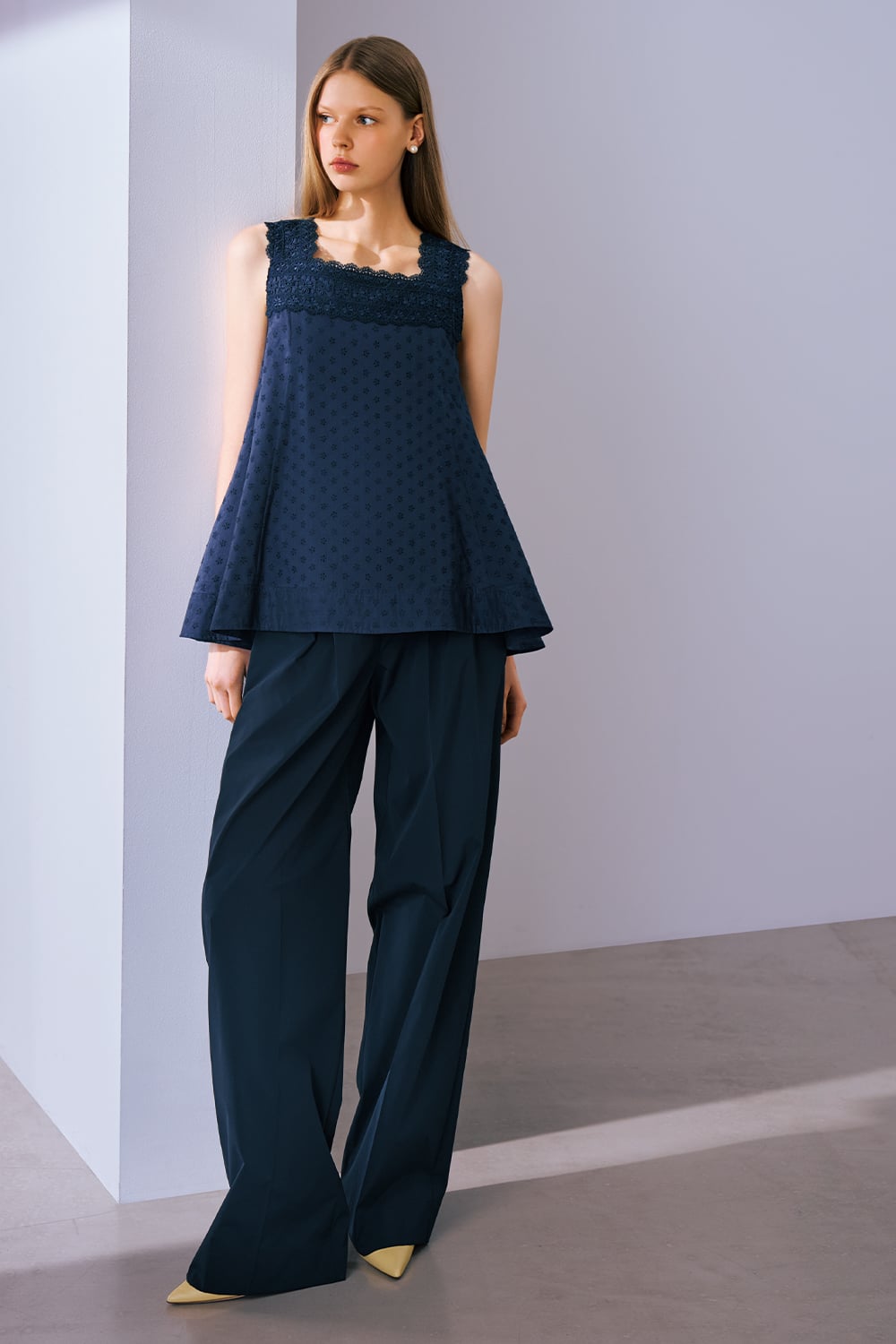 A model is wearing a navy sleeveless lace-trimmed top paired with navy wide-leg trousers and pointed heels.