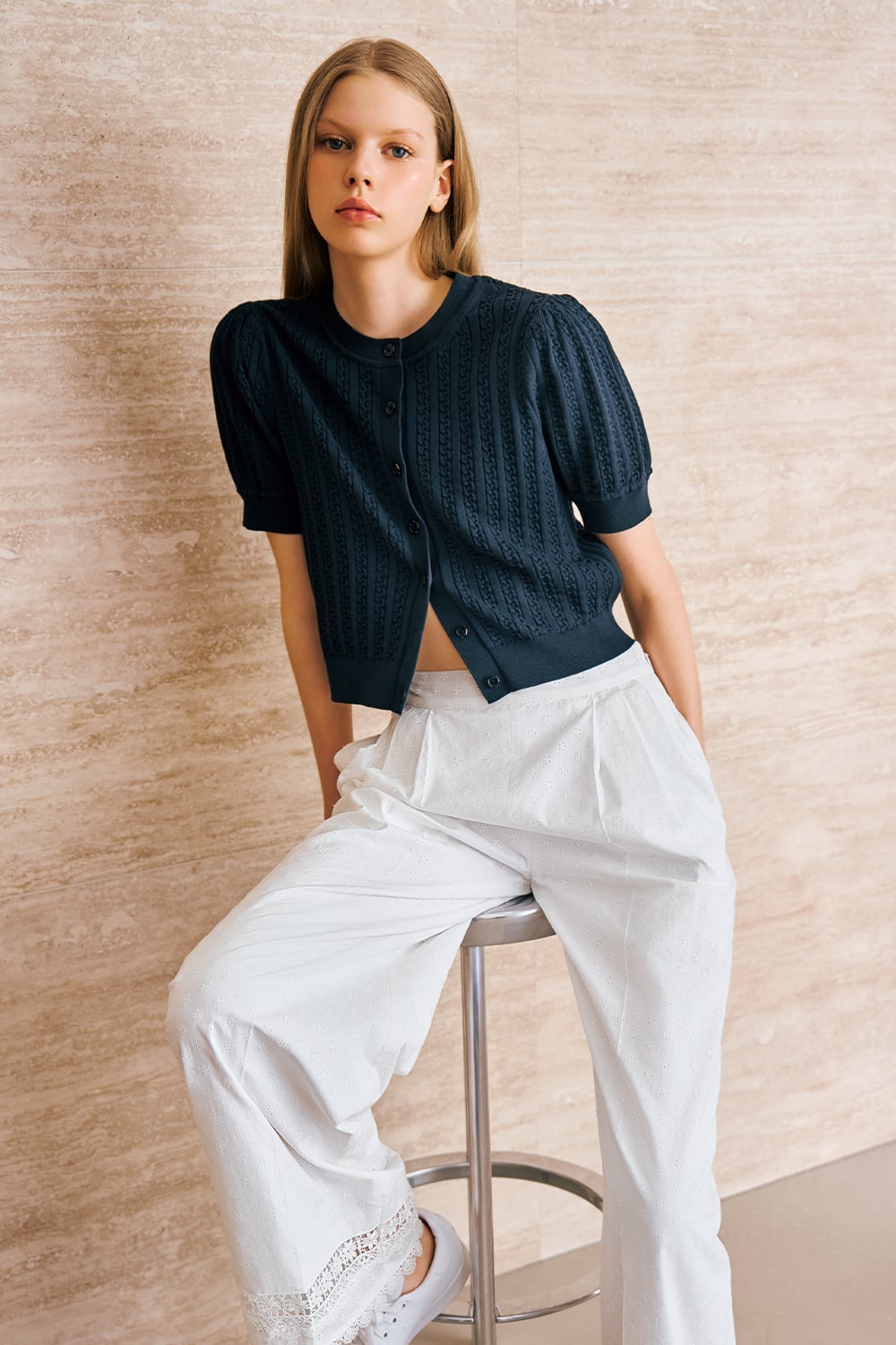 A model is wearing a navy short-sleeve knit cardigan paired with white wide-leg trousers and sneakers.
