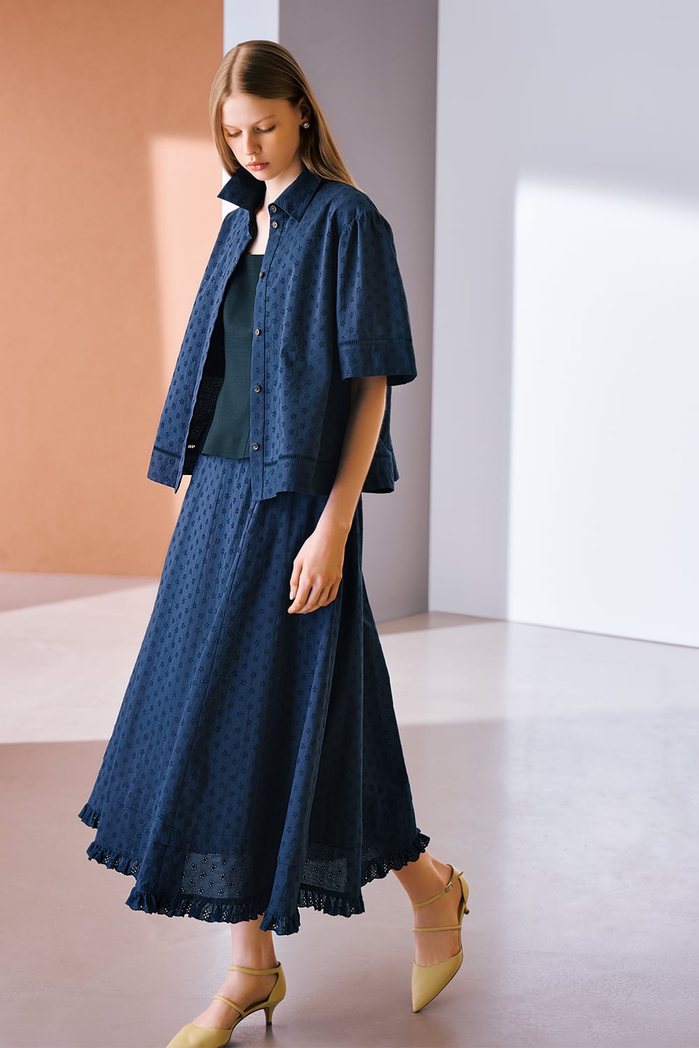 A model is wearing a navy short-sleeve shirt paired with a matching midi skirt and a dark-toned knit top.