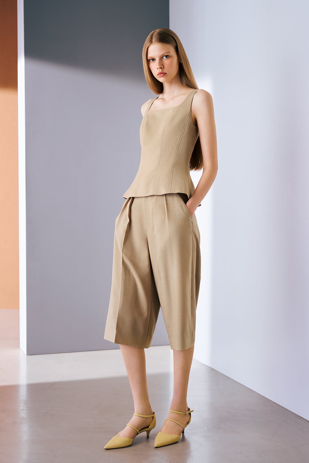 A model is wearing a beige sleeveless top paired with matching cropped wide-leg trousers and pointed heels.