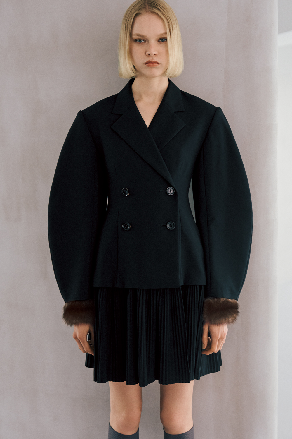 The model is wearing a black jacket and a black skirt.