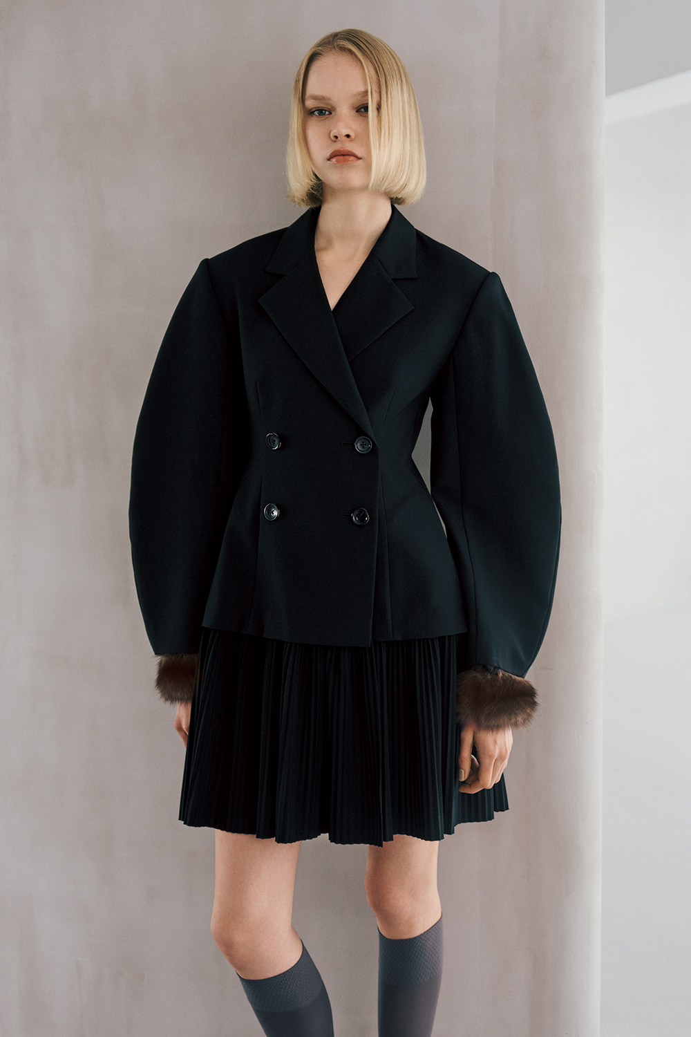 The model is wearing a black jacket and a black skirt.