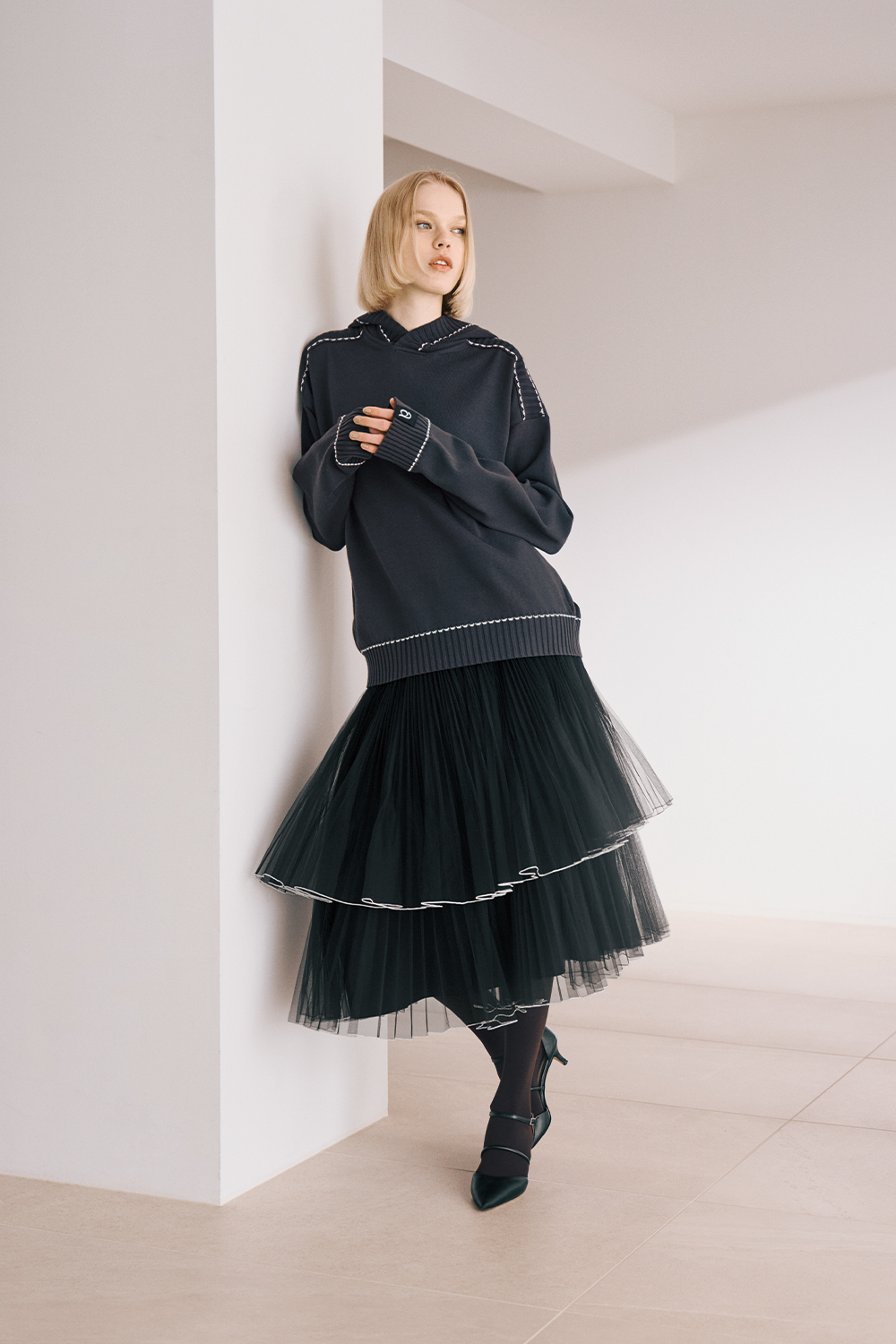 The model is wearing a black top and a black ruffled skirt.