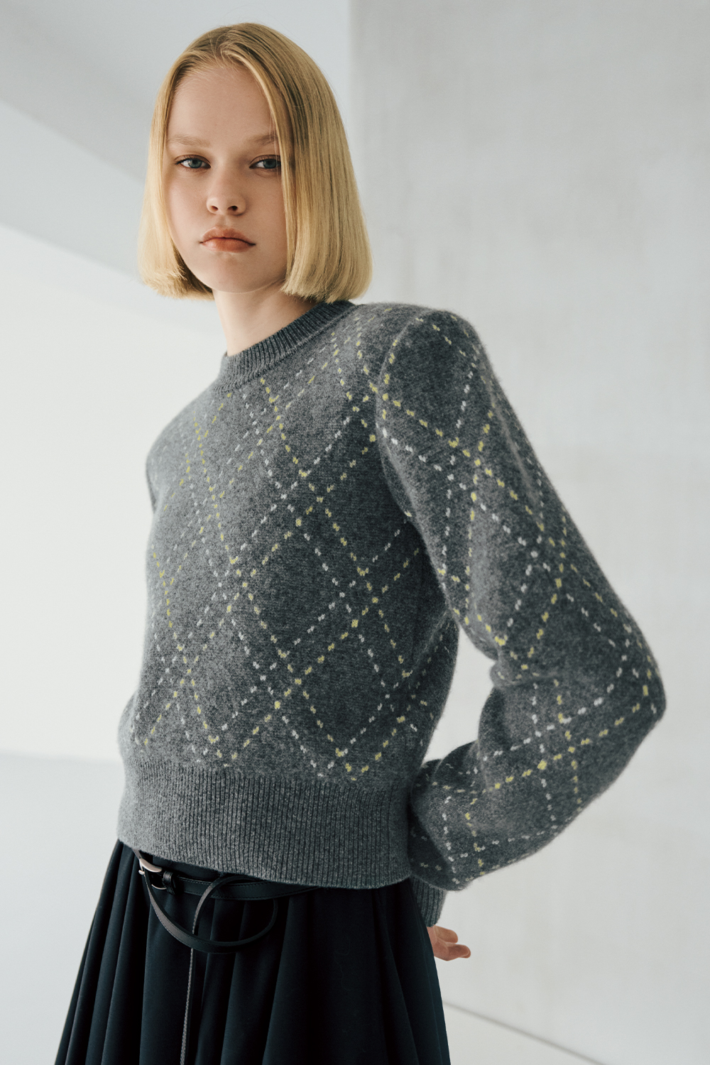 The model is wearing a grey patterned top and a skirt.