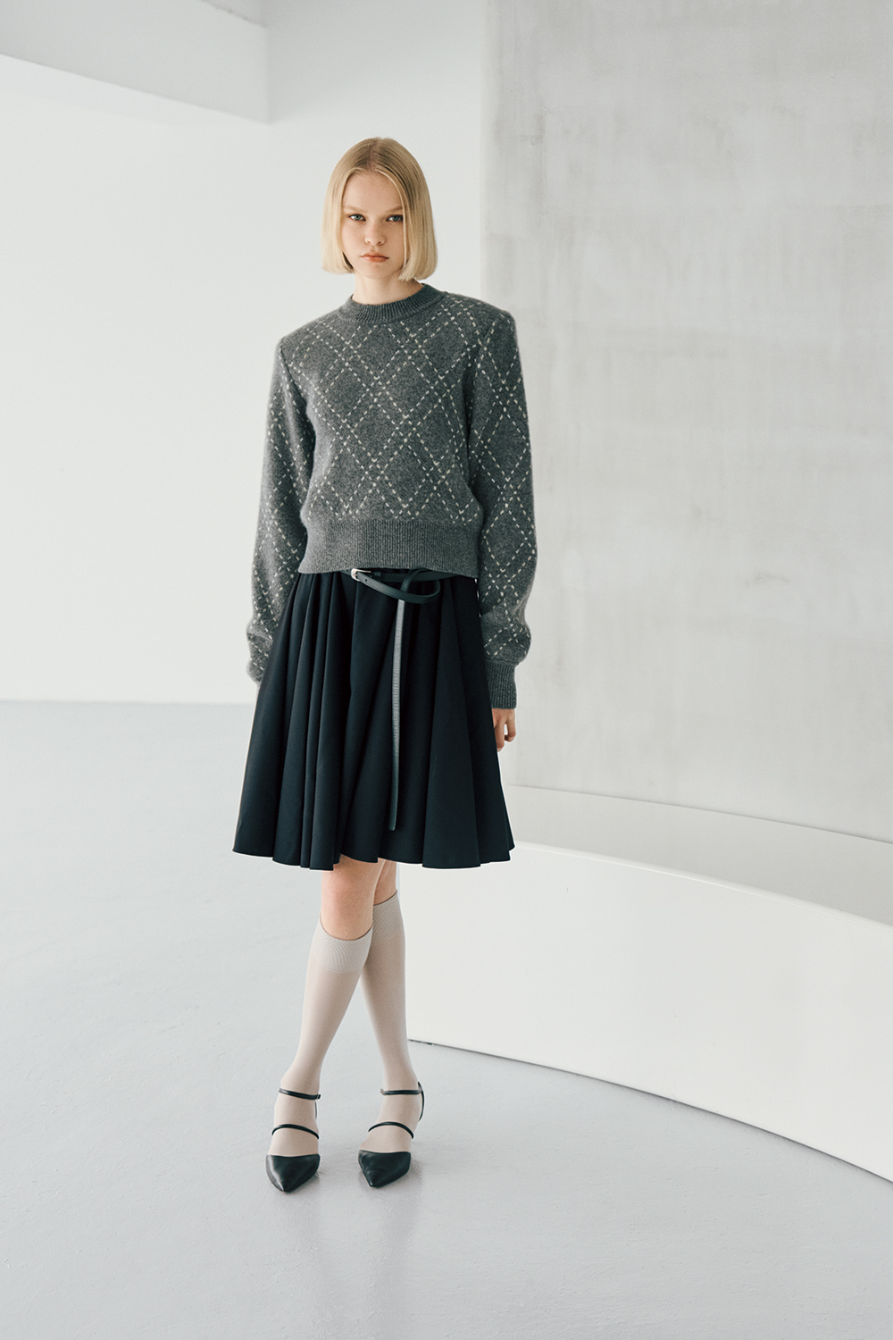 The model is wearing a grey patterned top and a skirt.