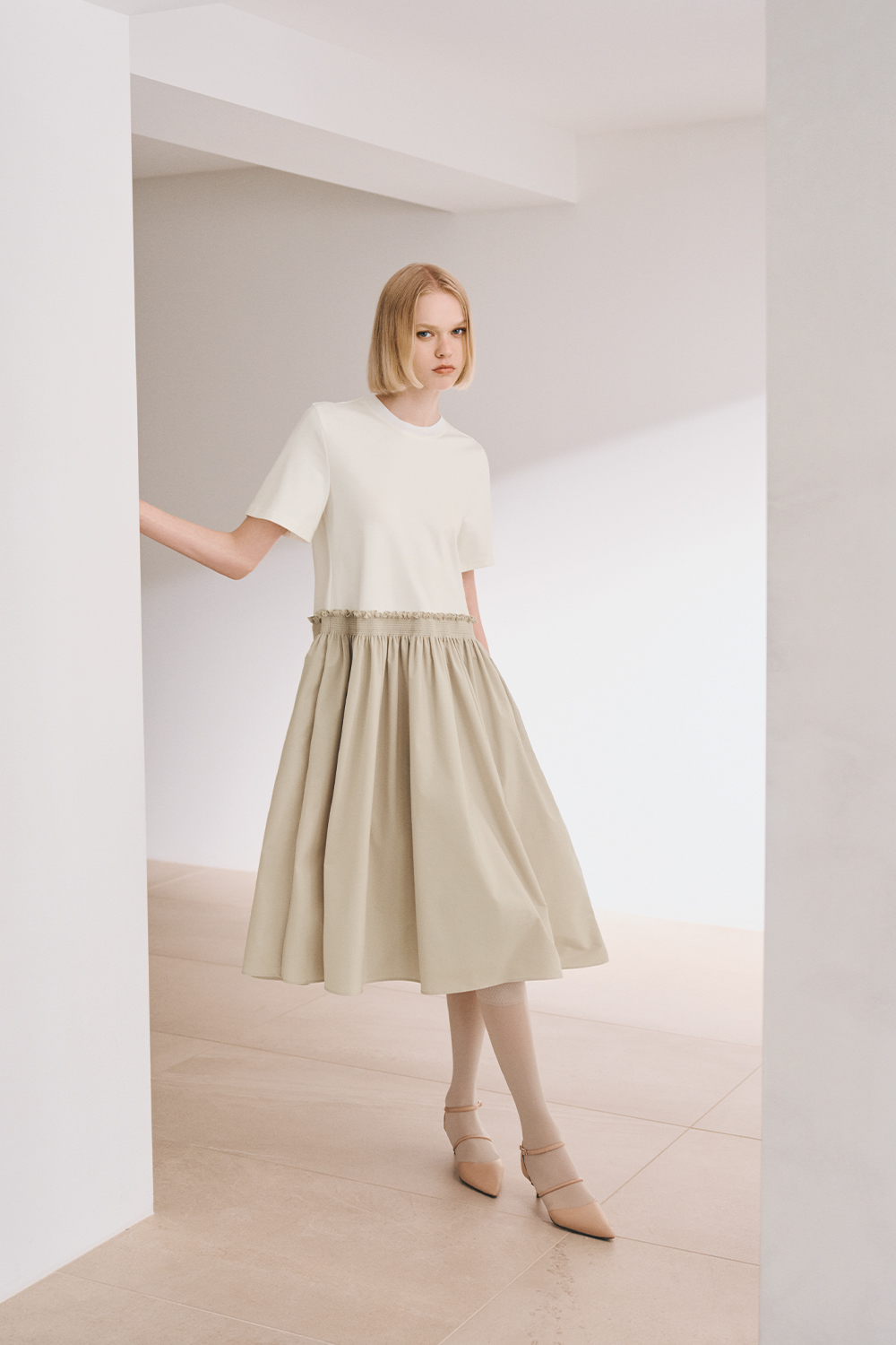 The model is wearing a white top and a beige skirt.