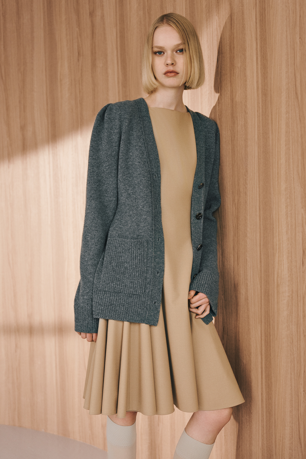 The model is wearing a gray knit and a beige dress.