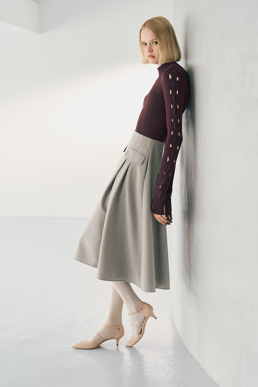The model is wearing a burgundy top and a grey skirt.