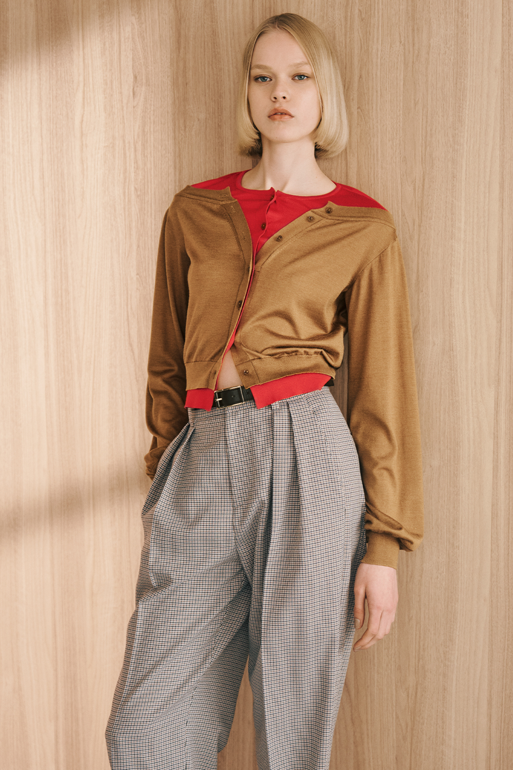 The model is wearing a brown jacket, a red top, and patterned pants.