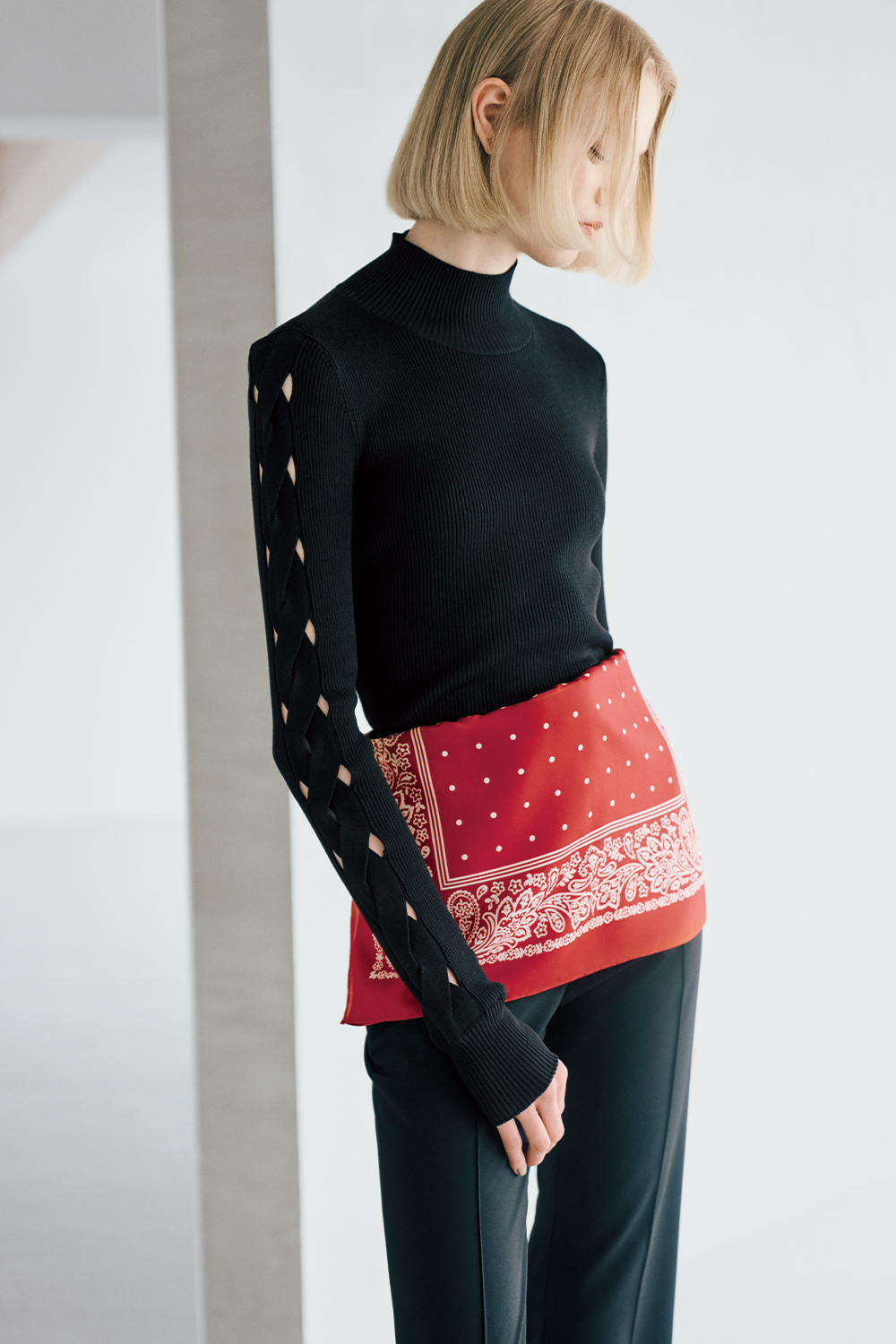 The model is wearing a black top, a red belt, and black pants.