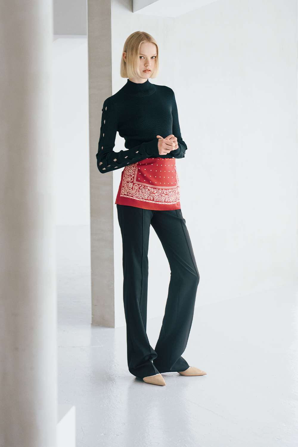 The model is wearing a black top, a red scarf, and black pants.