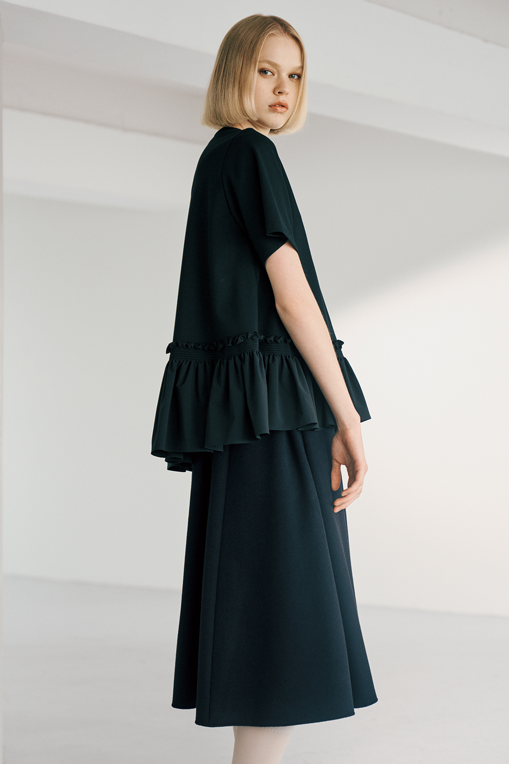 The model is wearing a black top and a black skirt.